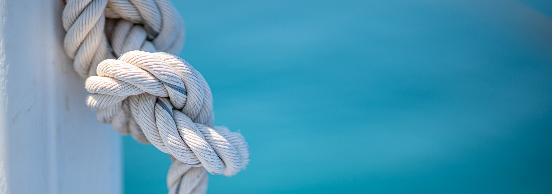 Psychotherapie-Angebot: Ein Tau mit einem Seemannsknoten hängt an einem Pfosten im Sonnenlicht. Dahinter erahnt man das türkise Meer. Der Knoten steht für die Schwierigkeiten des Patienten.