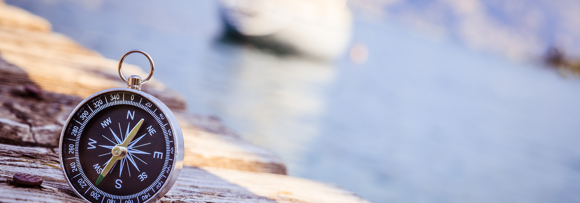 Ablauf einer Psychotherapie: Im Bild-Vordergrund: Ein Taschenkompass steht auf den Planken eines Stegs. Im Hintergrund ist unscharf das Heck eines ankernden Segelboots zu erkennen. Der Kompass dient als Sinnbild für Orientierung.