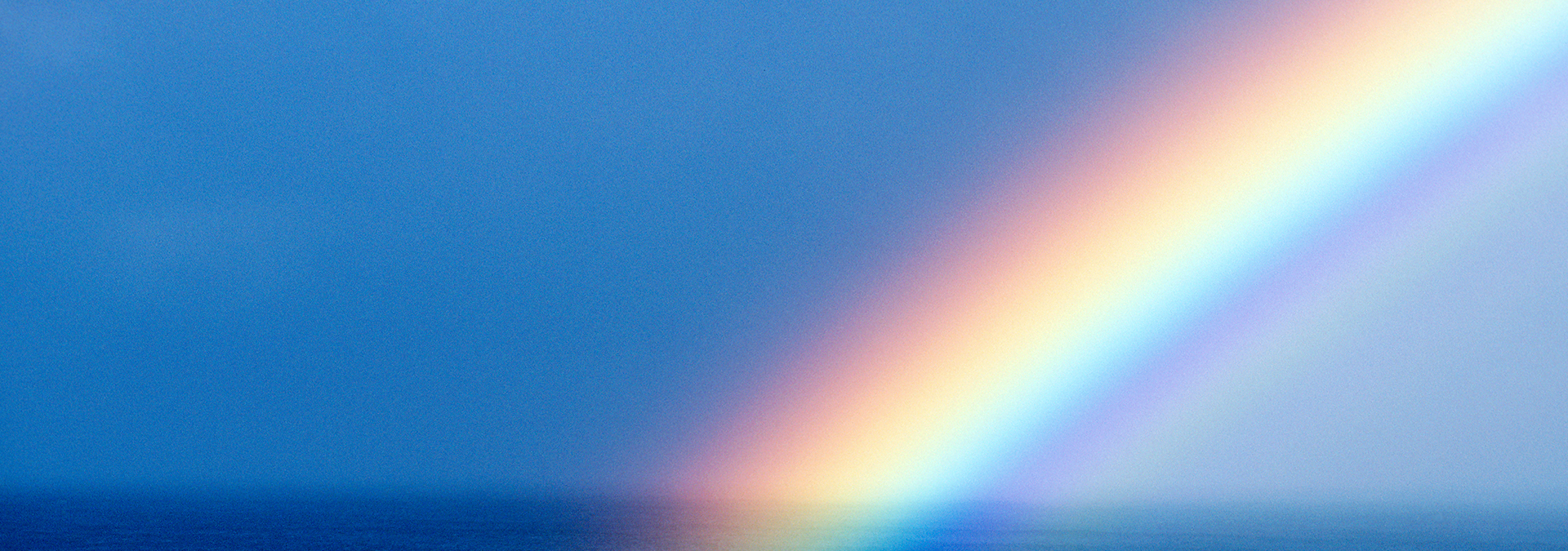 Psychotherapie-Angebot: Man sieht einen Regenbogen über dem dunklen Meer im Anschnitt. Der linke Teil des Himmels dahinter ist dunkel, nach rechts wird er heller. Der Regenbogen dient als Sinnbild für das Behandlungsspektrum.