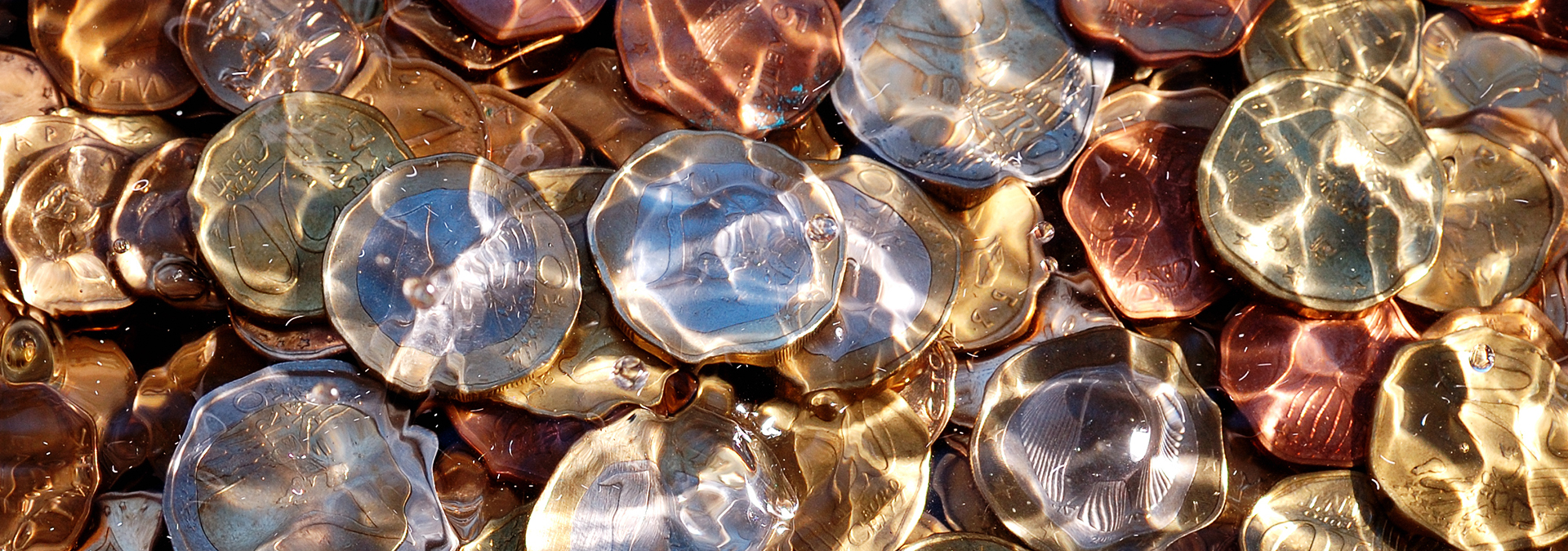 Kostenübernahme einer Psychotherapie: In einer Nahaufnahme sieht man Euromünzen unter spiegelndem Wasser im Sonnenlicht